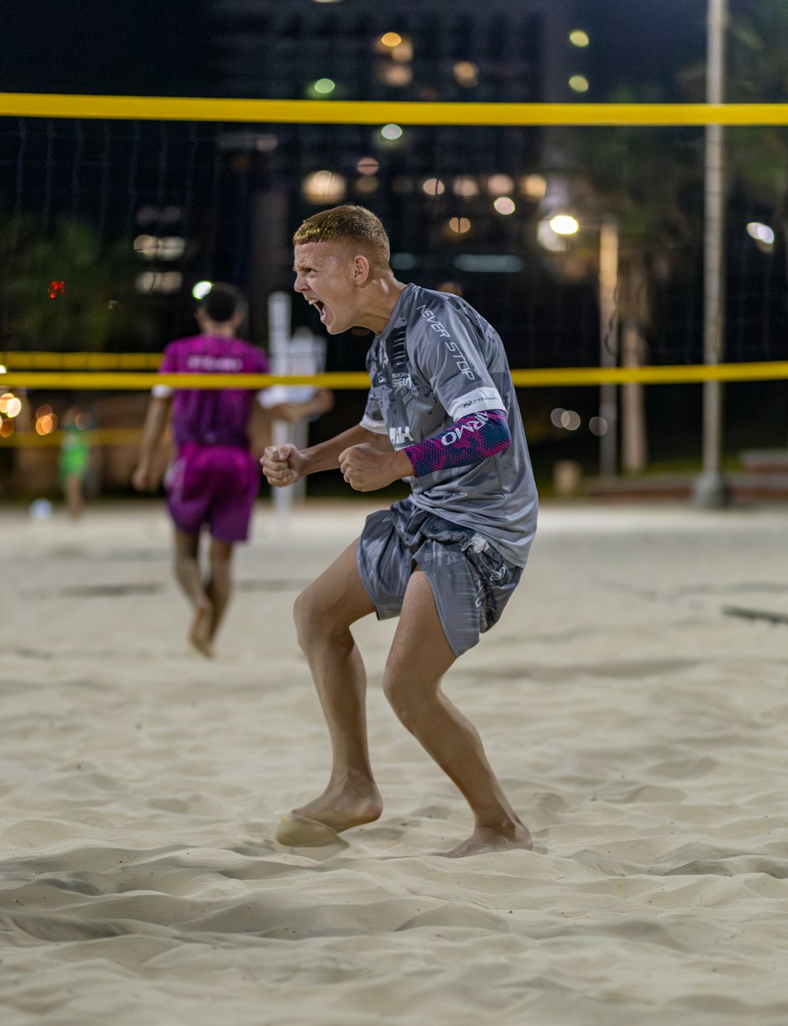 Beach volleyball player celebrates triumph on sandy court at night.