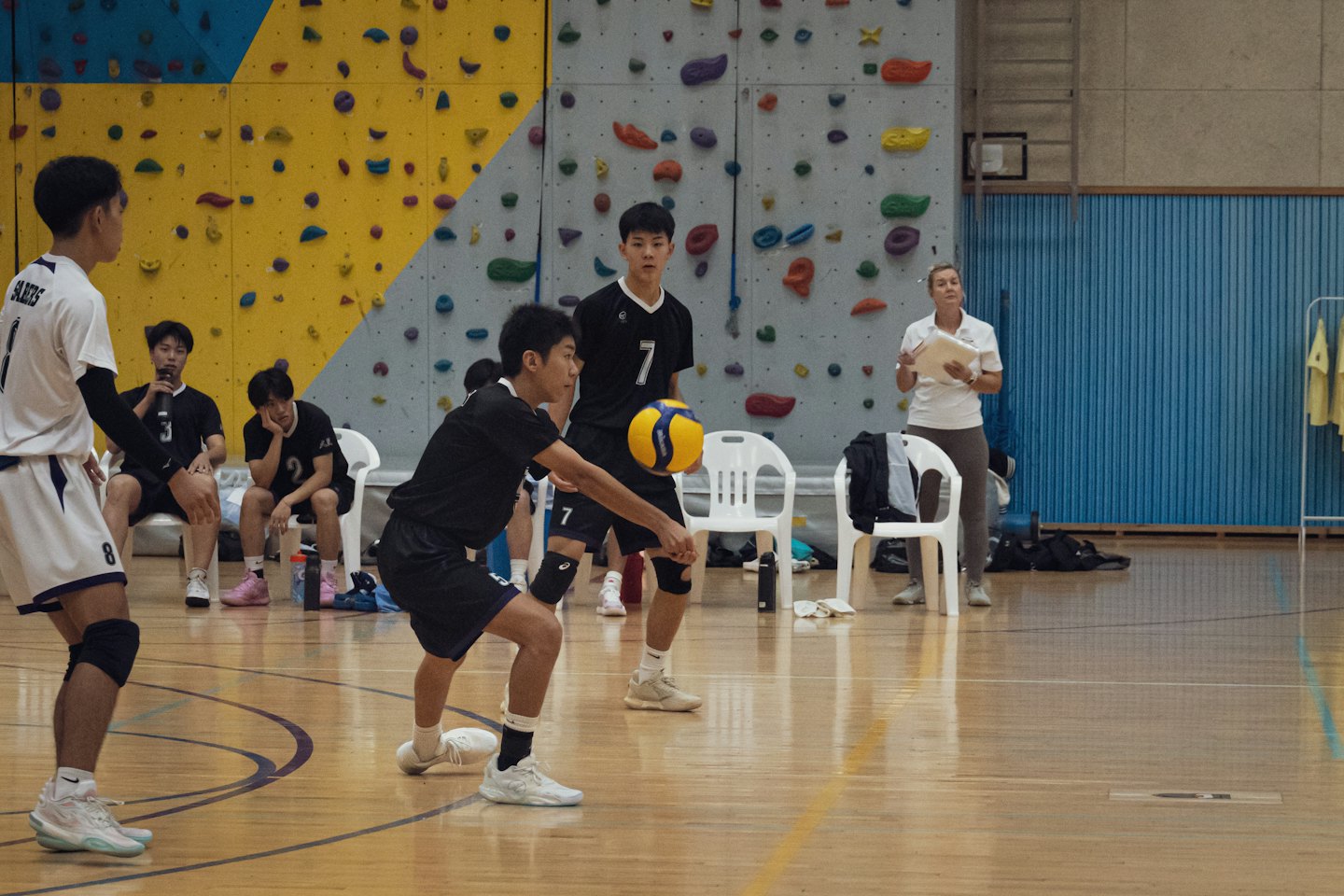Volleyball player serves a yellow and blue ball in a gymnasium.